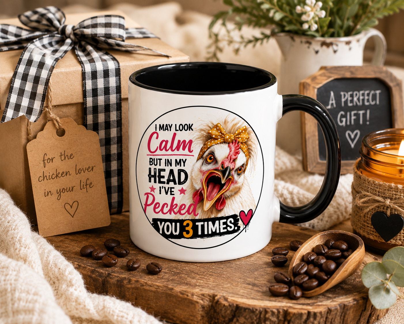 White 15 oz ceramic mug with black handle featuring Lucy the Silkie chicken and the saying "I May Look Calm But In My Head I've Pecked You 3 Times," displayed beside a wrapped farmhouse-style gift box with coffee beans, candle, greenery, and rustic décor for the perfect chicken lover gift.