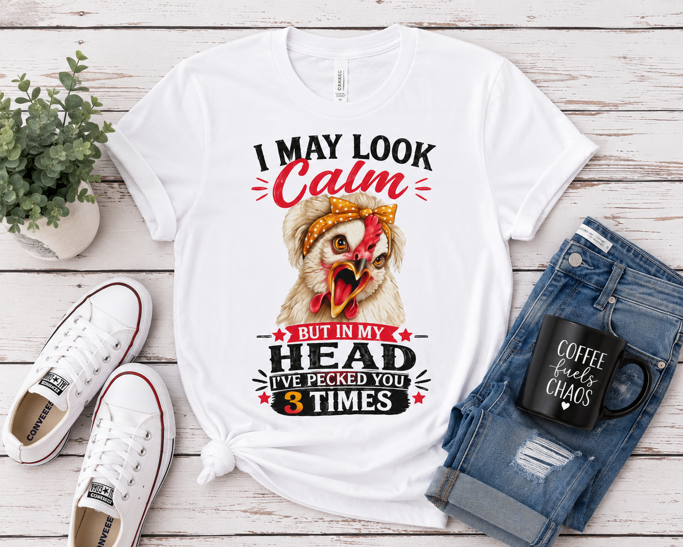 Flat lay of the "I May Look Calm" funny chicken graphic T-shirt by Woodland Willow Designs displayed with blue jeans, white sneakers, and farmhouse-inspired accessories on a rustic wood background. Features the Lucy & Friends™ design with the phrase "I May Look Calm... But In My Head I've Pecked You 3 Times."