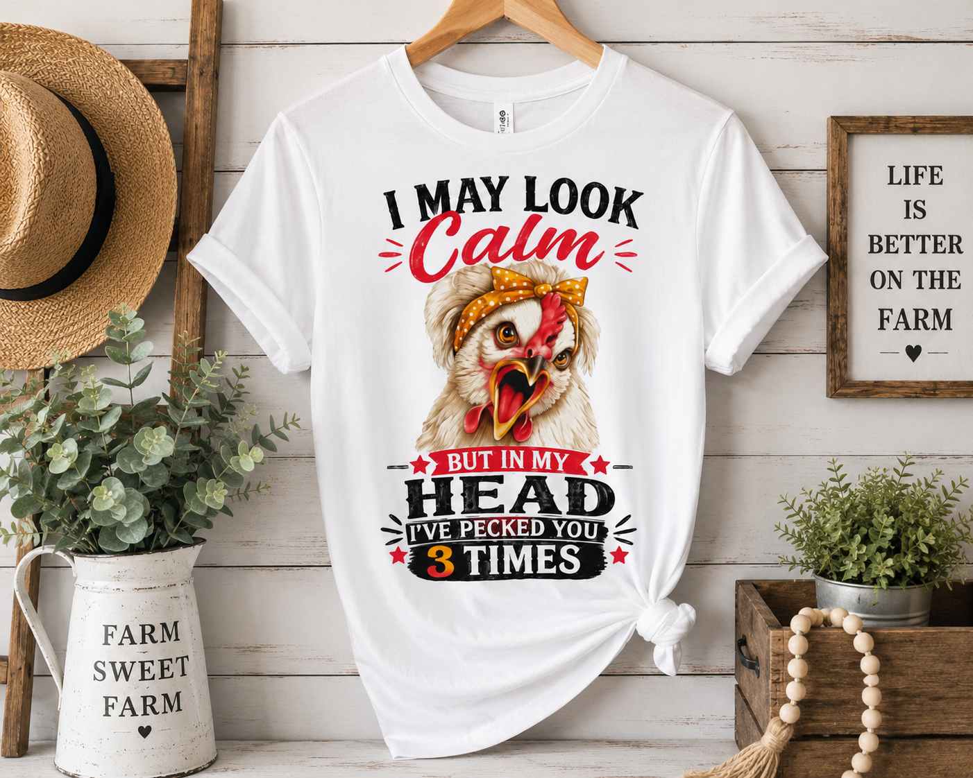 Farmhouse-style display of the "I May Look Calm" funny chicken graphic T-shirt by Woodland Willow Designs hanging on a wooden hanger against a rustic shiplap wall. Features the Lucy & Friends™ design with the phrase "I May Look Calm... But In My Head I've Pecked You 3 Times," surrounded by cozy farmhouse décor including greenery, a straw hat, and vintage country accents.