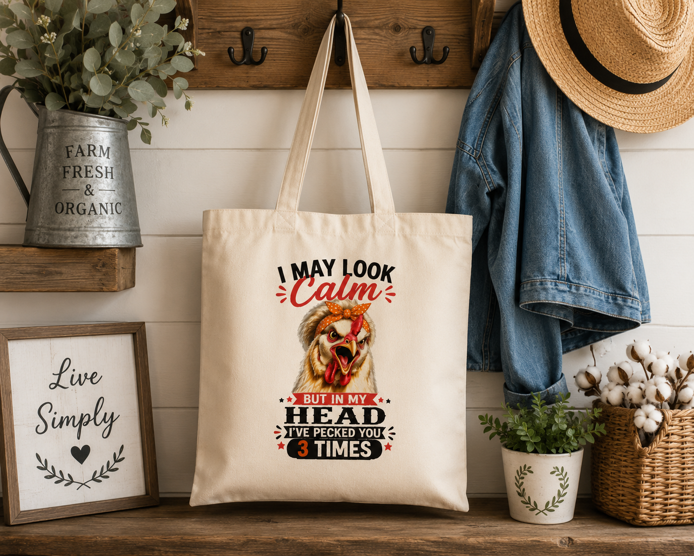 Farmhouse entryway display featuring the "I May Look Calm" funny chicken canvas tote bag by Woodland Willow Designs hanging from a rustic wooden wall rack alongside a denim jacket, straw hat, and greenery. Features the Lucy & Friends™ chicken artwork.